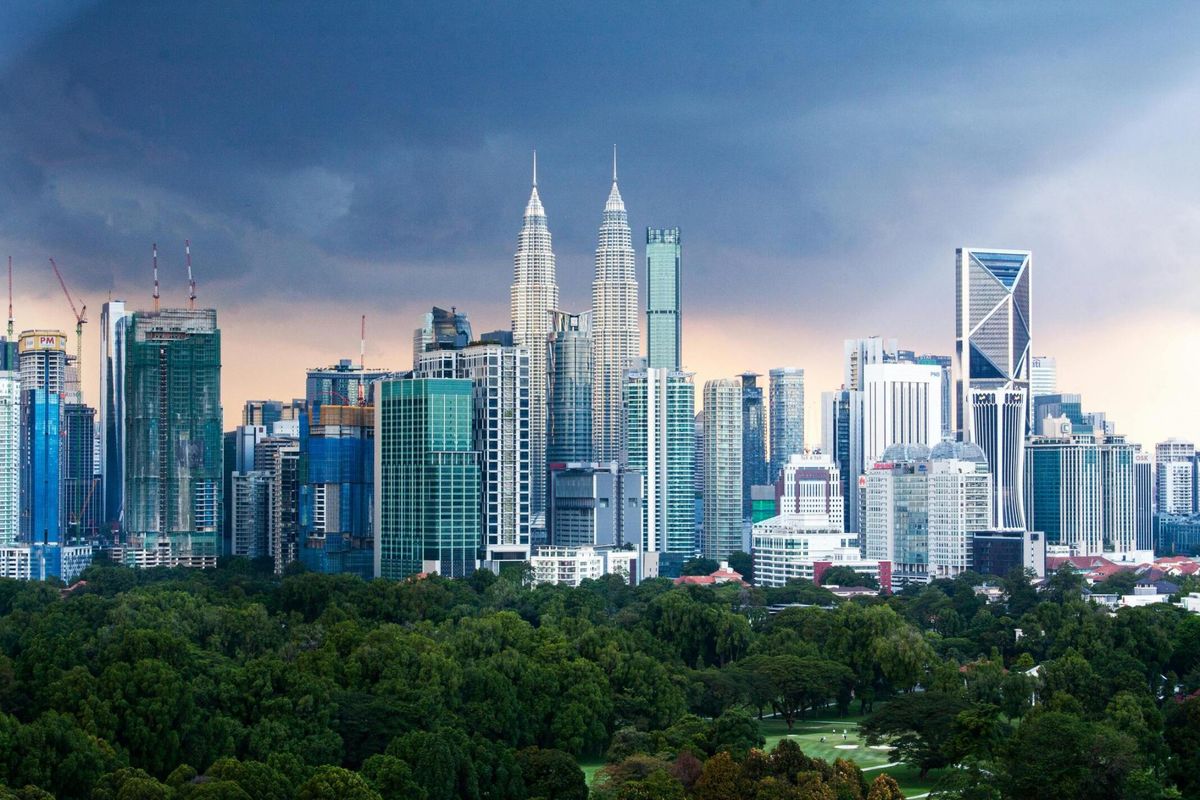 Modern city skyline with glass towers rising above tropical green canopy at dusk
